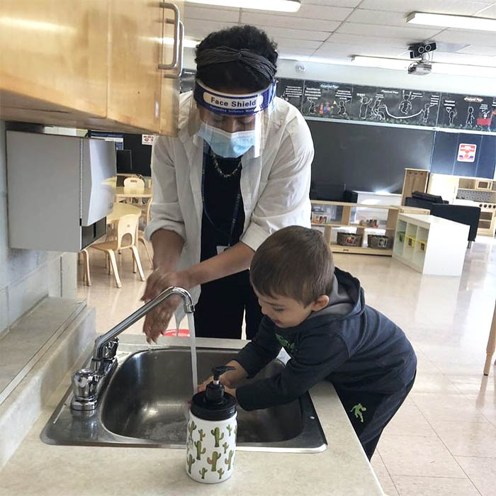 A PLASP staff member wearing a mask assists a child to wash his hands 